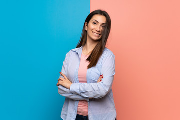 Young woman over pink and blue wall keeping the arms crossed in frontal position