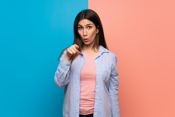 Fototapeta premium Young woman over pink and blue wall surprised and pointing front