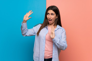 Young woman over pink and blue wall is a little bit nervous and scared