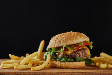 delicious meat burger with cheese, greenery and sesame near french fries isolated on black