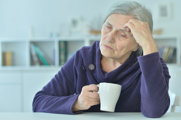 sad old woman with headache drinking tea