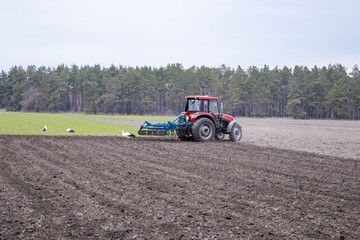 Obraz premium A farmer on a tractor prepares the land with a cultivator. Sowing on agricultural fields.