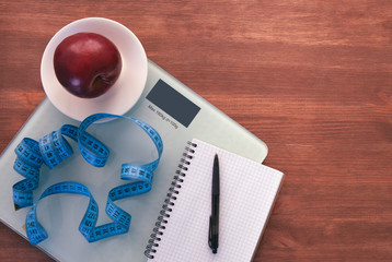The concept of healthy nutrition, fitness and weight loss. Weights, measuring tape, apple, open notebook and pencil on the table. 