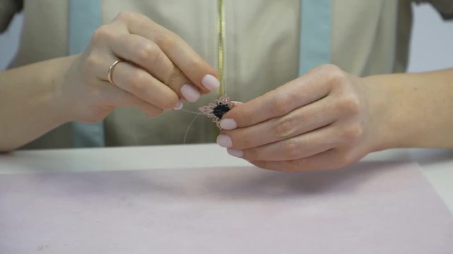 Needlework girl sews beads to brooch.