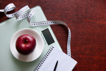 The concept of healthy nutrition, fitness and weight loss. Weights, measuring tape, apple, open notebook and pencil on the table. 