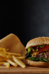 selective focus of delicious burger with meat and french fries on black background