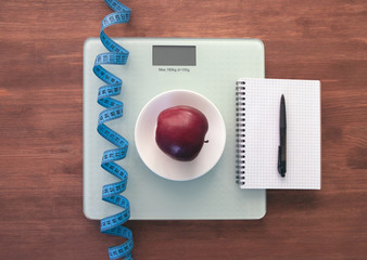 The concept of healthy nutrition, fitness and weight loss. Weights, measuring tape, apple, open notebook and pencil on the table. 