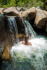 Girl swimming and relaxing in a waterfall in wild nature among big stones.