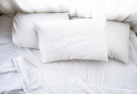 White sheets, blanket and pillows on the cozy bed with a window at the back. Bedding concept.