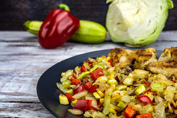 Vegetable cabbage, peppers, zucchini and fried chicken wings on a plate on a wooden background. Healthy food.