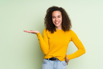 Dominican woman over isolated green background holding copyspace imaginary on the palm to insert an...