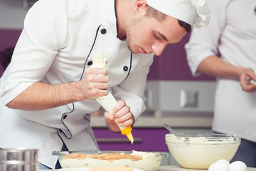 Obraz na płótnie Canvas Tiramisu cooking, passing exam concept. Portrait of serious concentrated trainee in cook uniform making italian dessert in modern kitchen. Indoor shot