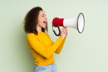 Dominican woman over isolated green background shouting through a megaphone