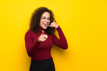 Dominican woman with turtleneck sweater making phone gesture and pointing front