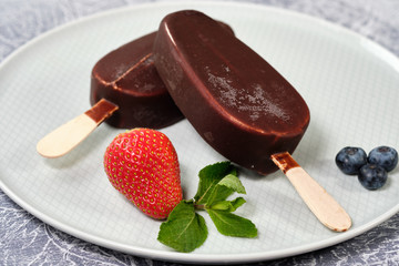 chocolate butter ice cream popsicles on the white plate with fresh summer berries, strawberries, blueberries