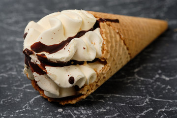 vanilla ice cream in waffle cone with chocolate icing on dark grey background