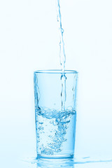 Pouring water into glass on white background. Water spilled on the table.