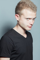 Obraz premium Portrait of funny smiling young man with short blond hair and freckles on face wearing black t-shirt and posing over gray background. Hipster style. Studio shot