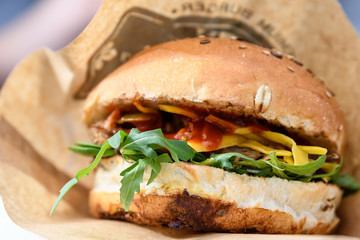Close up of a fresh burger with pulled meat, cheese and fresh arugula leaves in a fresh bun with seeds, on brown paper for sale at a street food festival