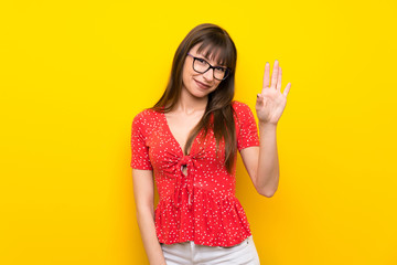 Young woman over yellow wall saluting with hand with happy expression