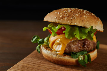 close up of tasty meat burger with cheese and greenery on wooden chopping board
