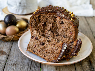 Amazing Chocolate Easter Cake with chocolate drops and dry cherries on an old wooden background with black and golden eggs. Slice of cake. Easter concept. Selective focus, close up.