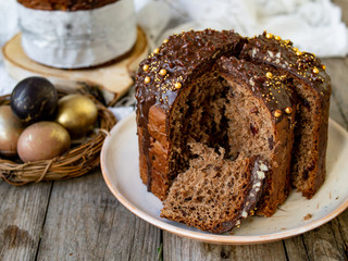 Amazing Chocolate Easter Cake with chocolate drops and dry cherries on an old wooden background with black and golden eggs. Slice of cake. Easter concept. Selective focus, close up.