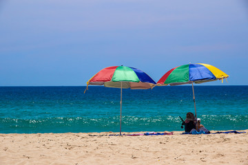 Two colorful umbrellas on white sand beach.