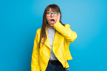 Young woman with yellow jacket on blue background with surprise and shocked facial expression