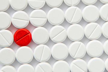 Top view of a pile of white medicine pills on a white surface. One tablet of red medication. Vaccine concept