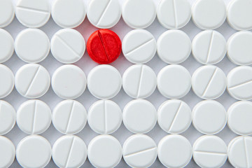 Top view of a pile of white medicine pills on a white surface. One tablet of red medication. Vaccine concept