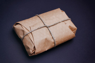Brown craft package wrapped with hemp cord on black background. 