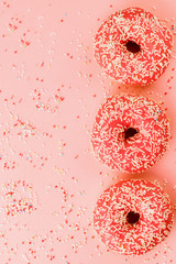 Three coral donuts. Donuts with icing on pink background.