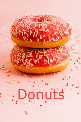 Two coral donuts standing in a line. Donuts decorated with icing