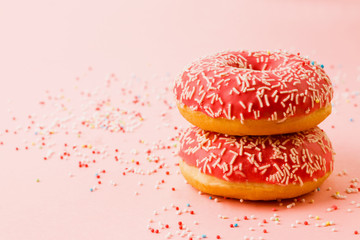 Two coral donuts standing in a line. Donuts decorated with icing