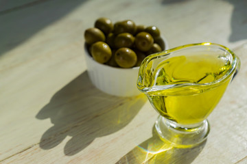 glass sauceboat with extra virgin olive oil and fresh green olives on wooden table.