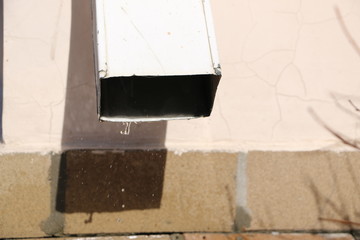 spring thaw drops on  Sunny day. melted snow flows from  gutter to  asphalt.