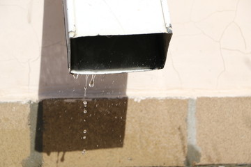 spring thaw drops on  Sunny day. melted snow flows from  gutter to  asphalt.