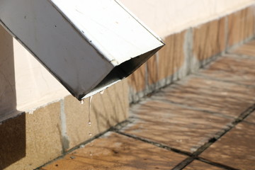 spring thaw drops on  Sunny day. melted snow flows from  gutter to  asphalt.