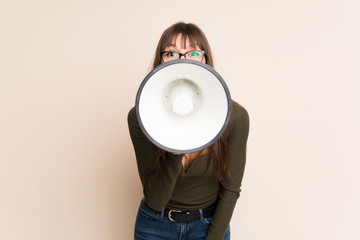 Young woman on ocher background shouting through a megaphone