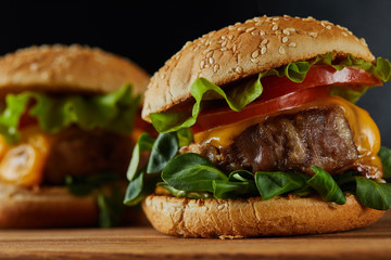 selective focus of delicious meat burgers with cheese and vegetables on wooden chopping board