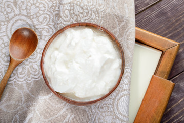 White yogurt in wooden bowl on linen towel on wooden table.