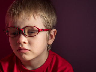 Funny child in red sweater on red background actively expresses emotions. Close up little kid boy in glasses posing front of camera