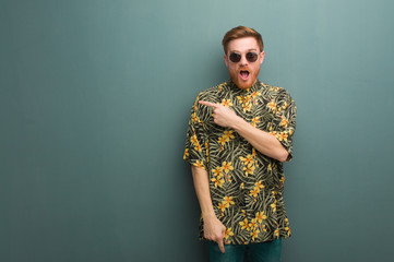 Young redhead man wearing exotic summer clothes pointing to the side