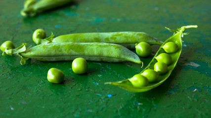 green peeled peas pods  in a spoon on a green background.