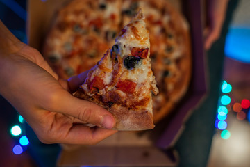 A slice of vegetarian pizza in female hands with blurred whole pizza in box on the laps, bokeh...