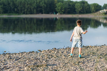 Fototapeta na wymiar a child, a teenager, on a stony shore throws stones into the river, lake