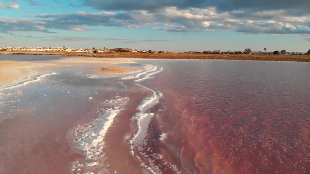 Das rote Wasser der Salzlagune von Torrevieja aus der Luft bei Wind und Wolken