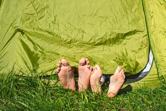 Two pairs of legs and heels stick out from green tent on a grassy glade meadow