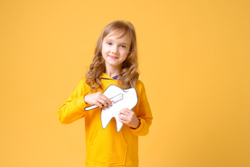 Little cute girl with toothbrush and dental layout in hand isolated on yellow background. Concept of health, oral hygiene, people and beauty. Layout of the space. Selective focus.